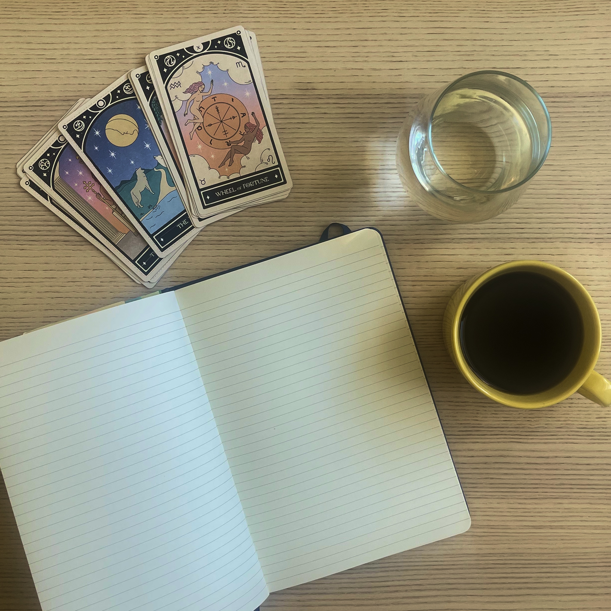Tarot cards, a journal, and coffee laid out on a wooden table